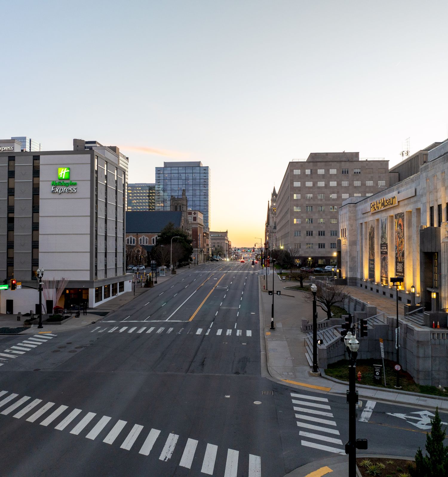 An empty city street at dawn with buildings and crosswalks on both sides, and a clear sky in the background.